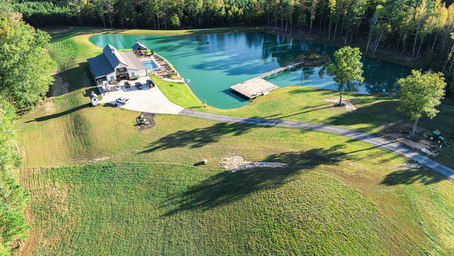 Aerial view of a residential backyard with a swimming pool and landscaped lawn surrounded by lush green trees.