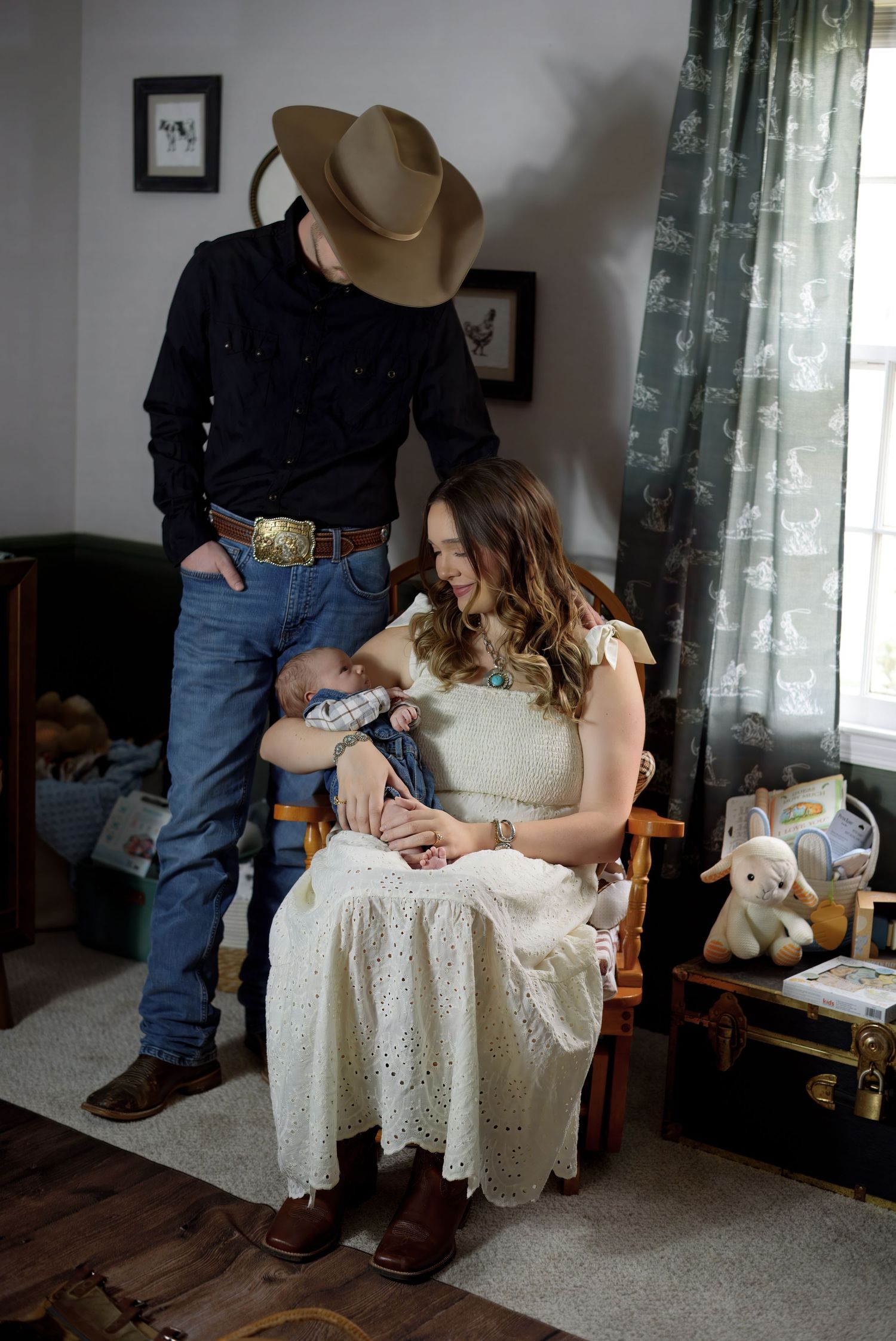 Photo showing a mother in a white lace dress holding and nursing a newborn baby in a home setting.