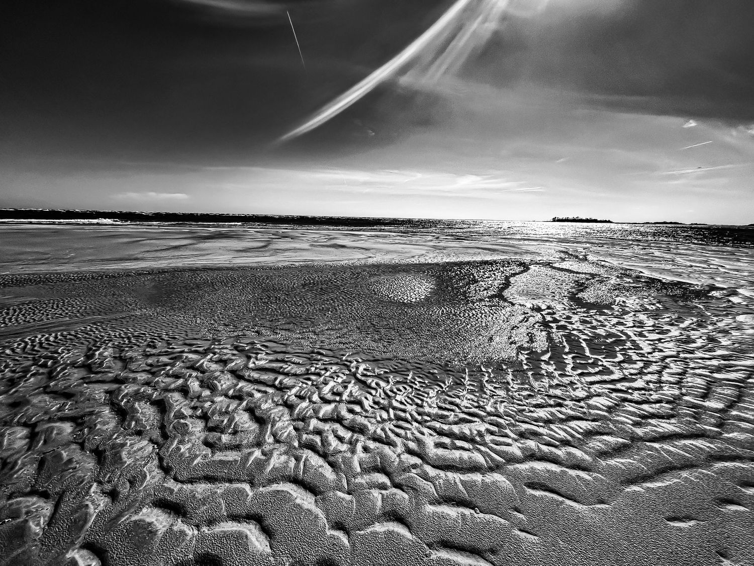 Black and white aerial view of textured sand ripples on a beach during low tide.