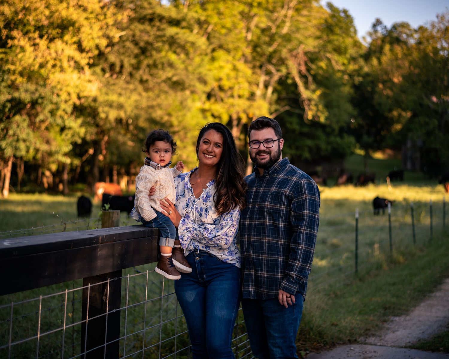 Family portrait session at golden hour along a rustic fence in a countryside setting.