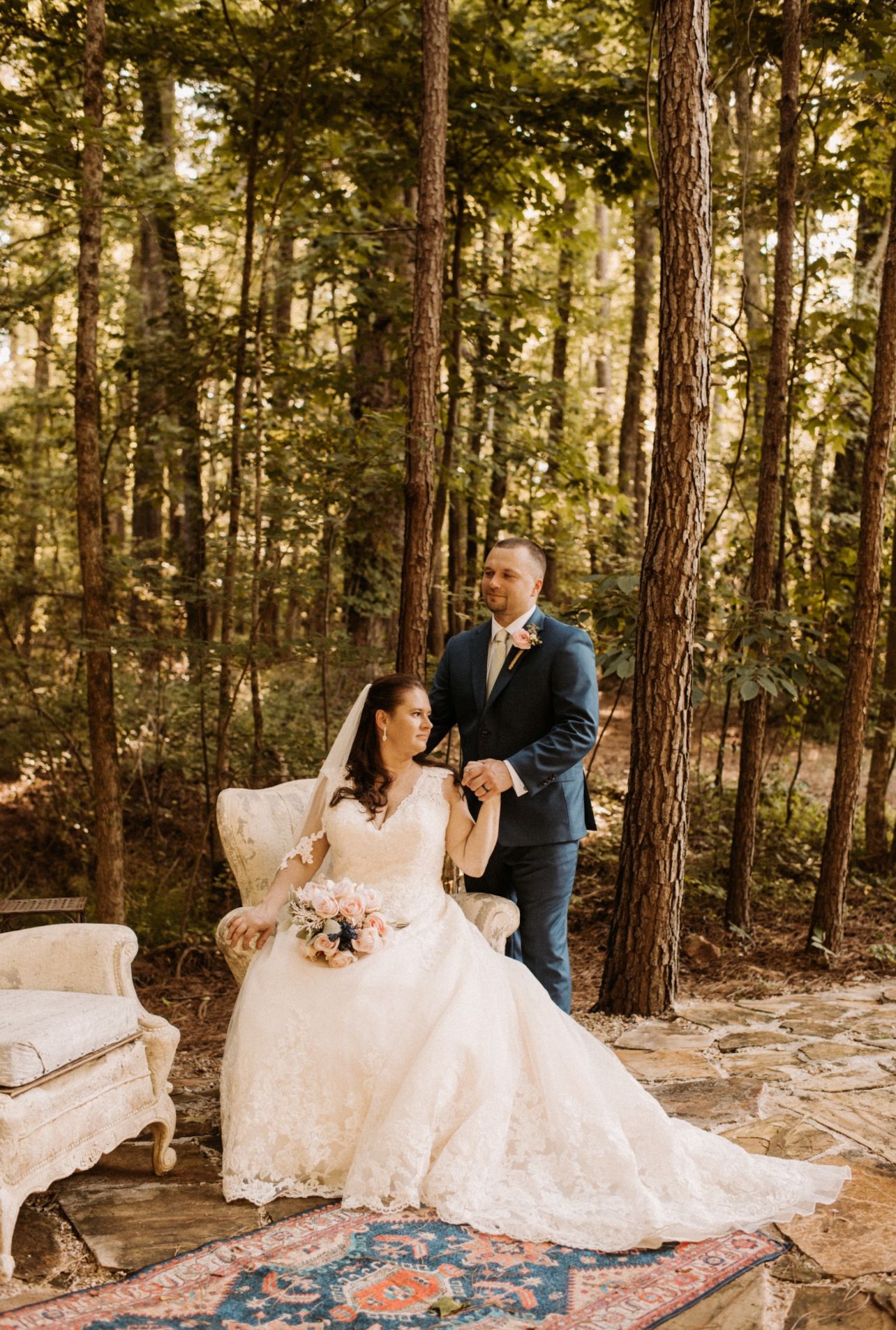 A romantic wedding photoshoot in a forest with a couple on a vintage rug among pine trees.