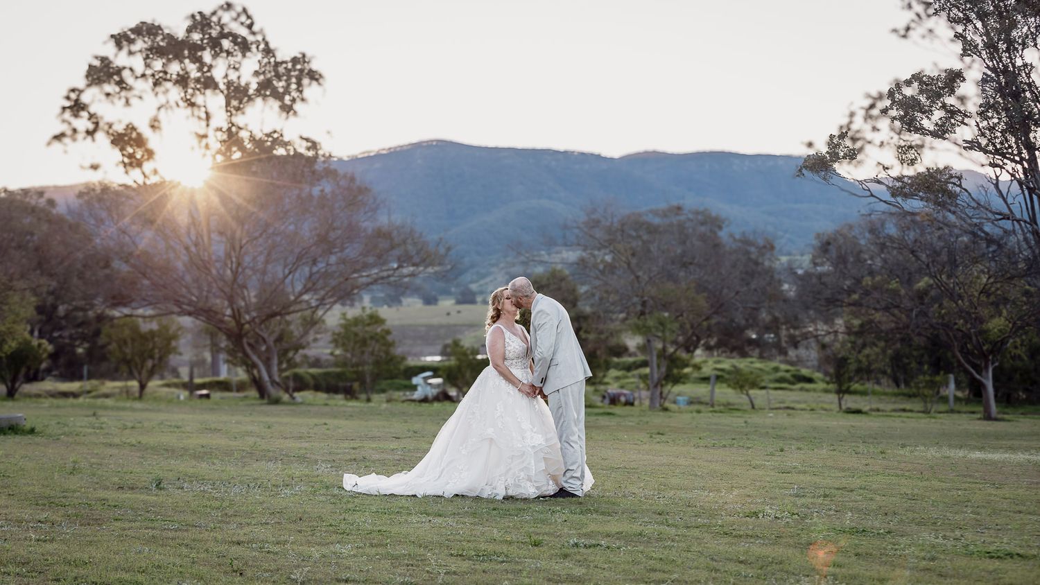 Scenic outdoor wedding photography session at sunset with mountains and trees in the background.