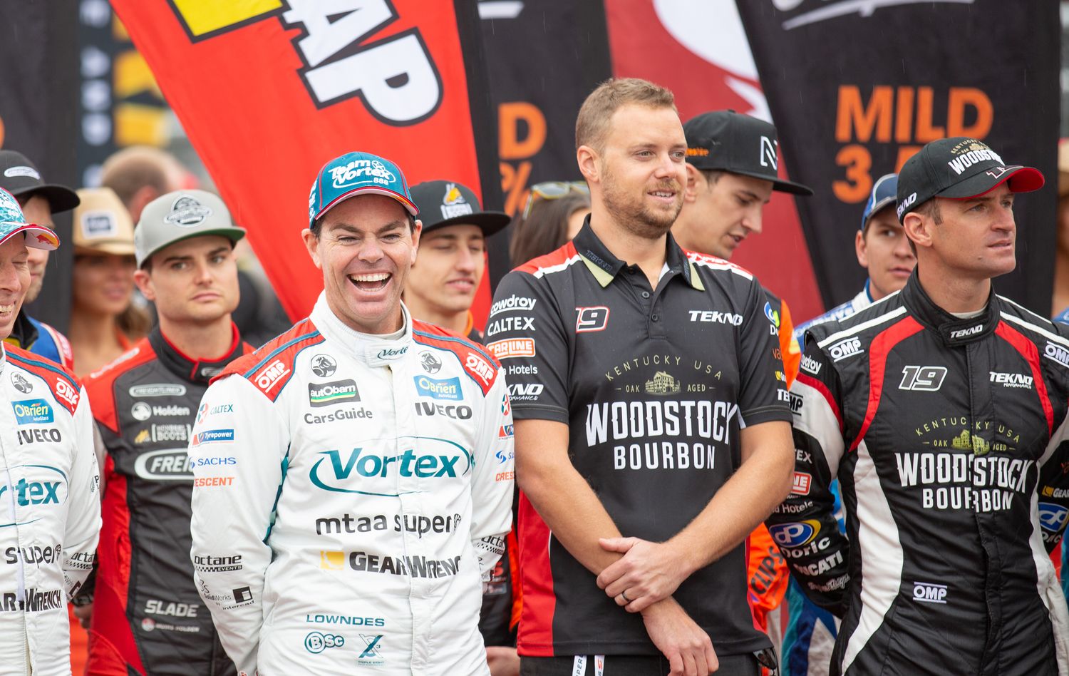 Group of professional racing drivers lined up for a promotional photo at motorsport event.