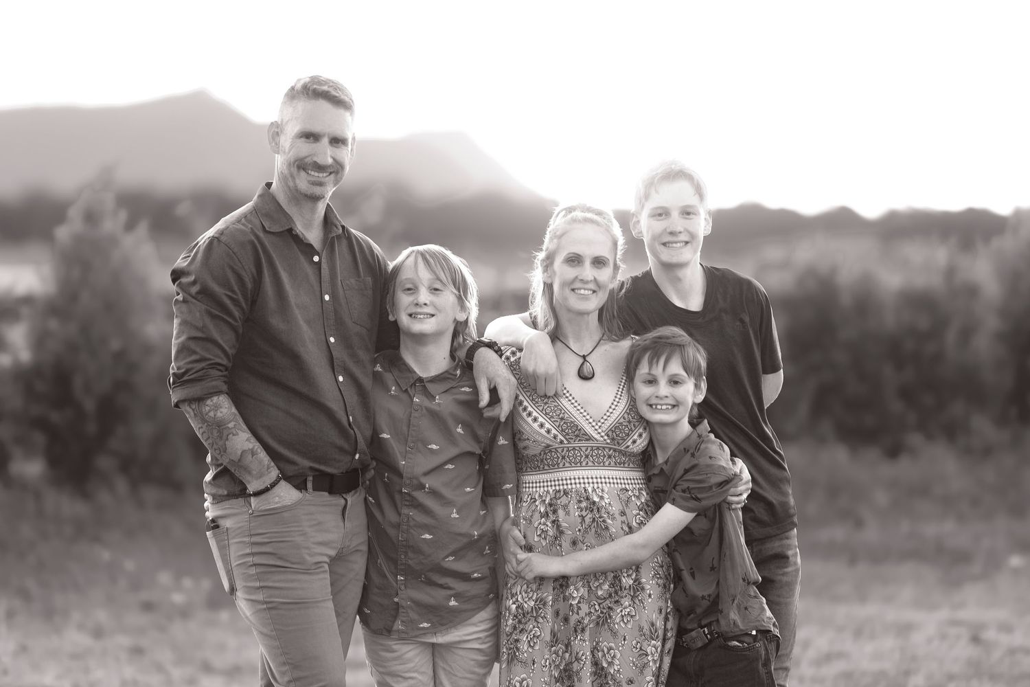 Group posing in an outdoor field during golden hour with mountains in the background.