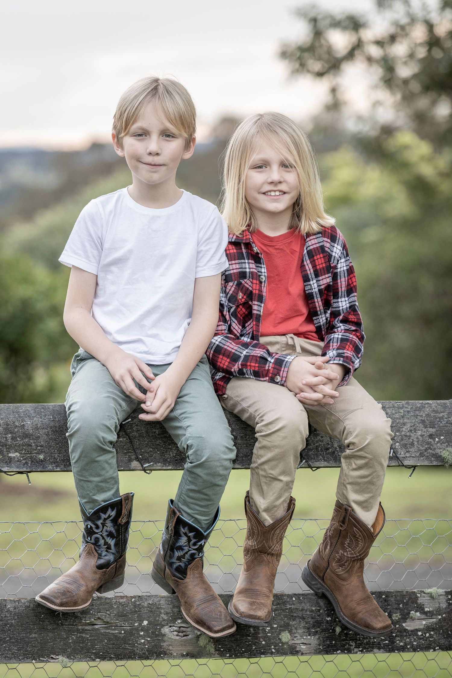 Two pairs of legs in boots sitting side by side on a stone wall outdoors.
