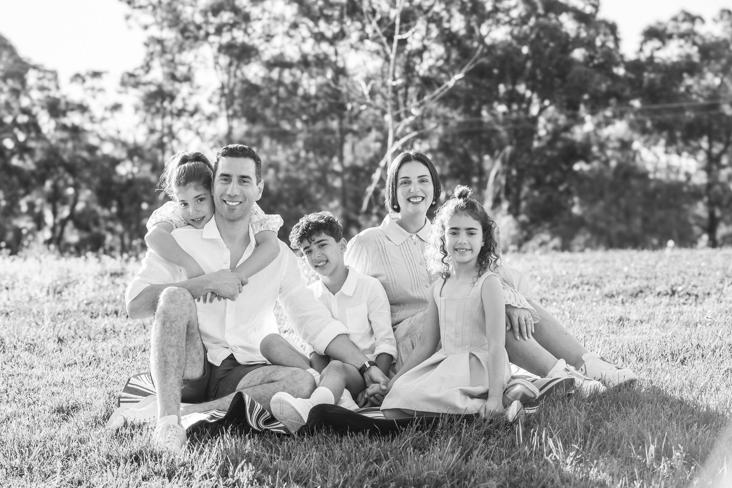 Black and white photo of a family sitting together on a grassy hillside with eucalyptus trees in the background.
