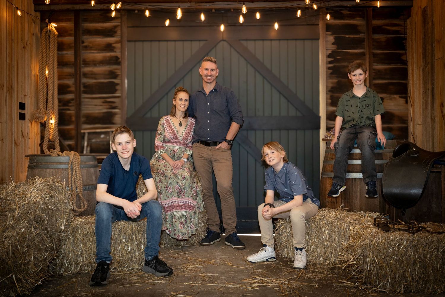 A series of casual family portraits taken in a rustic barn setting with hay bales and wooden backgrounds.
