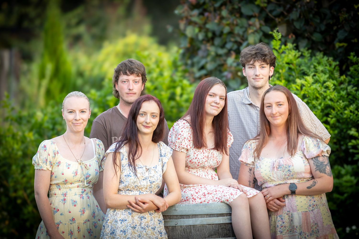 A group in coordinating floral dresses poses together in a lush garden setting during summer.