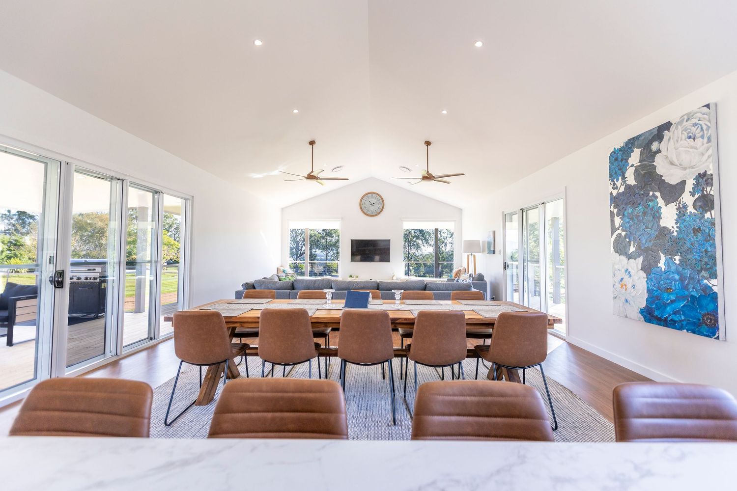 Modern coastal dining room with brown leather chairs, white walls, glass doors and abstract blue artwork.