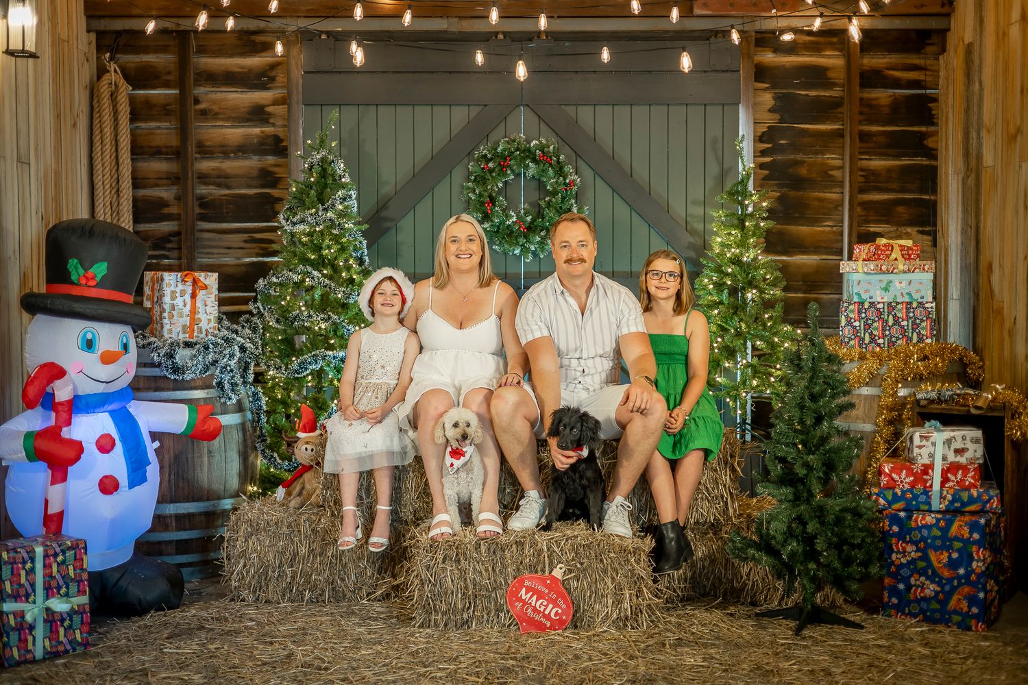 Family sitting on rustic wooden porch steps decorated with Christmas lights and festive holiday decorations.