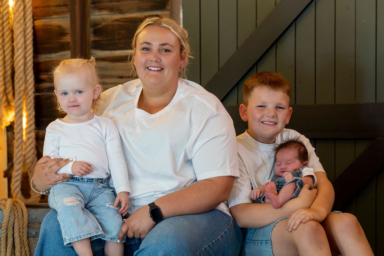 A family sits together on rustic wooden steps in coordinated white and blue casual outfits.