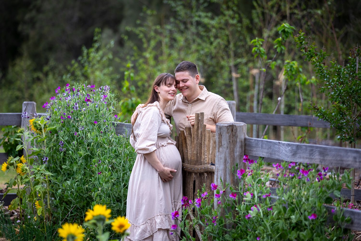 A romantic couple embraces in a lush garden setting with blooming flowers and greenery.