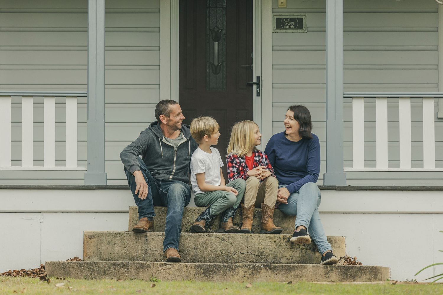 Groups sitting casually on concrete steps outside a gray weatherboard house.
