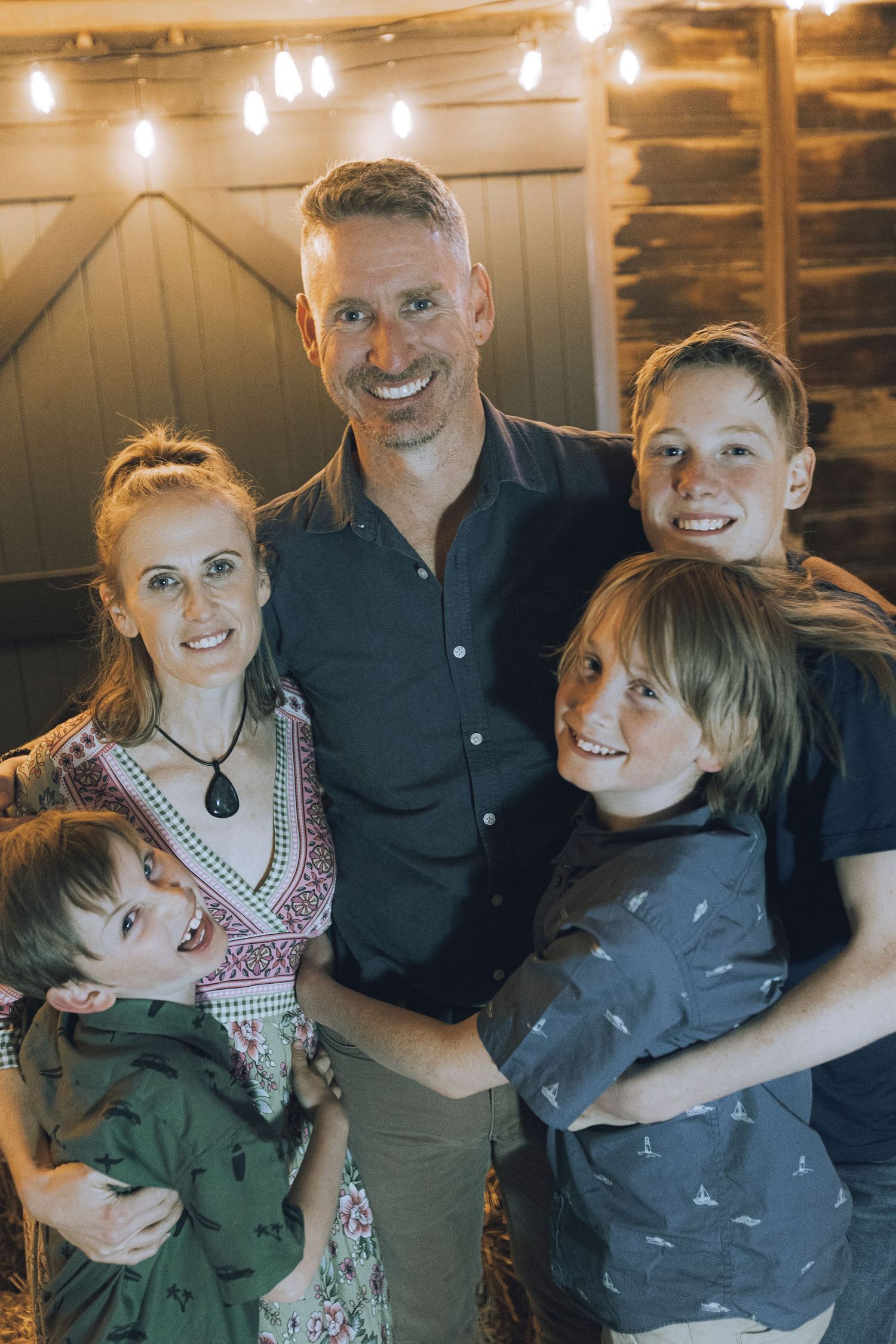 A family poses together in a rustic barn setting with warm lighting and wooden walls in the background.