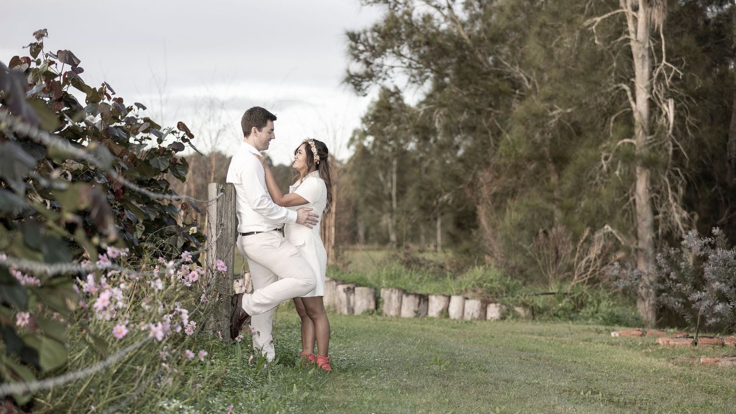 A couple shares an intimate moment on a grassy hillside path surrounded by eucalyptus trees and spring flowers.