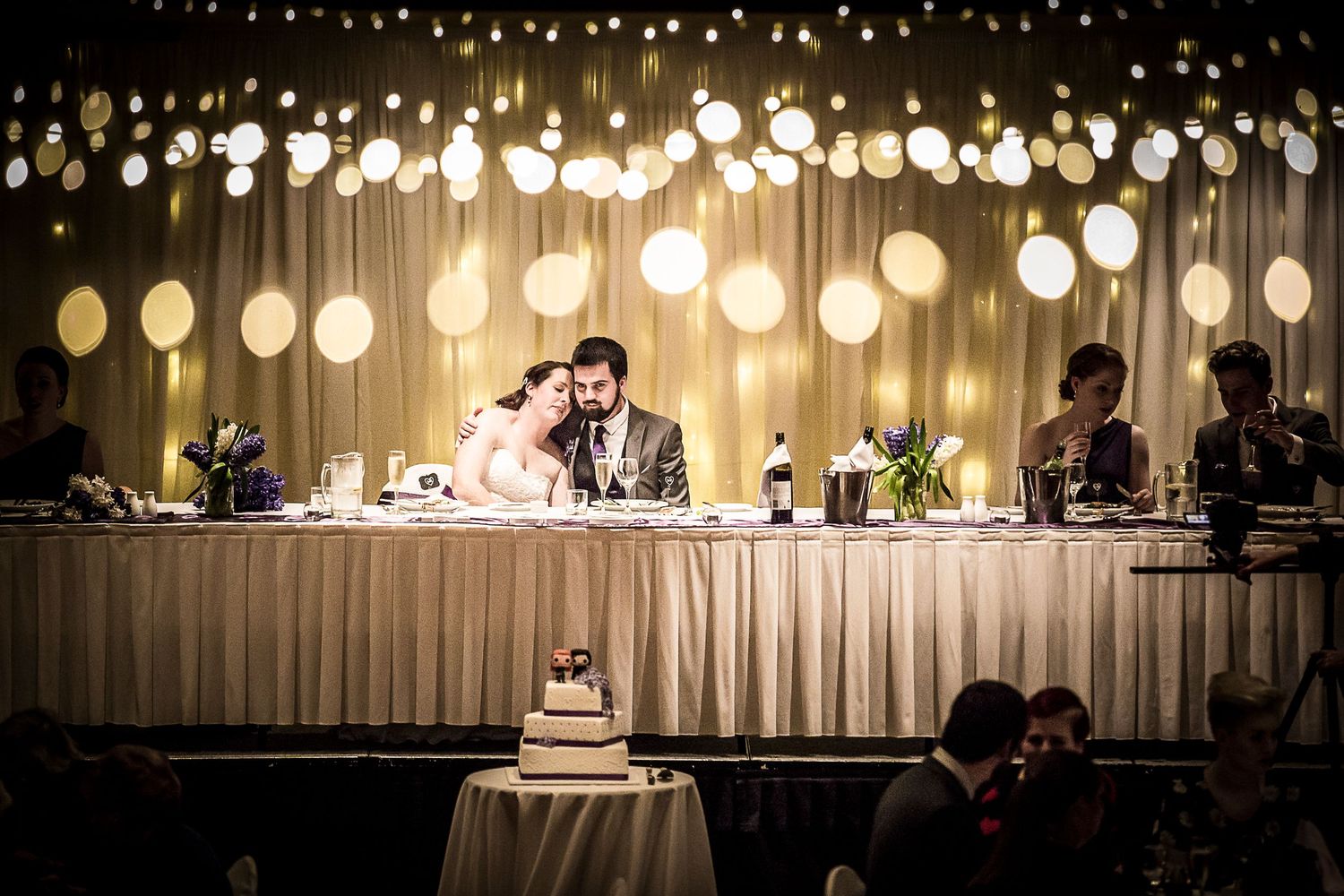 A romantic wedding reception scene with glowing paper lanterns hanging above the bridal party table.
