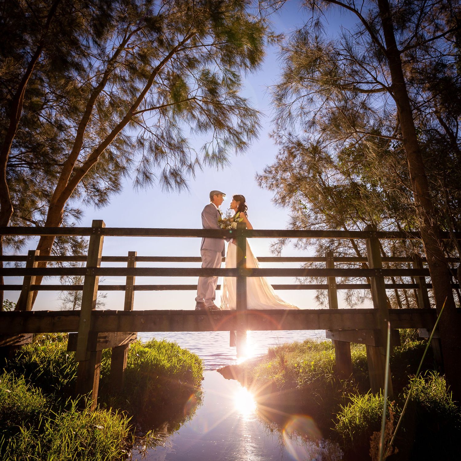 Scenic sunset view through trees and wooden railings overlooking a tranquil lake with sunburst effect.