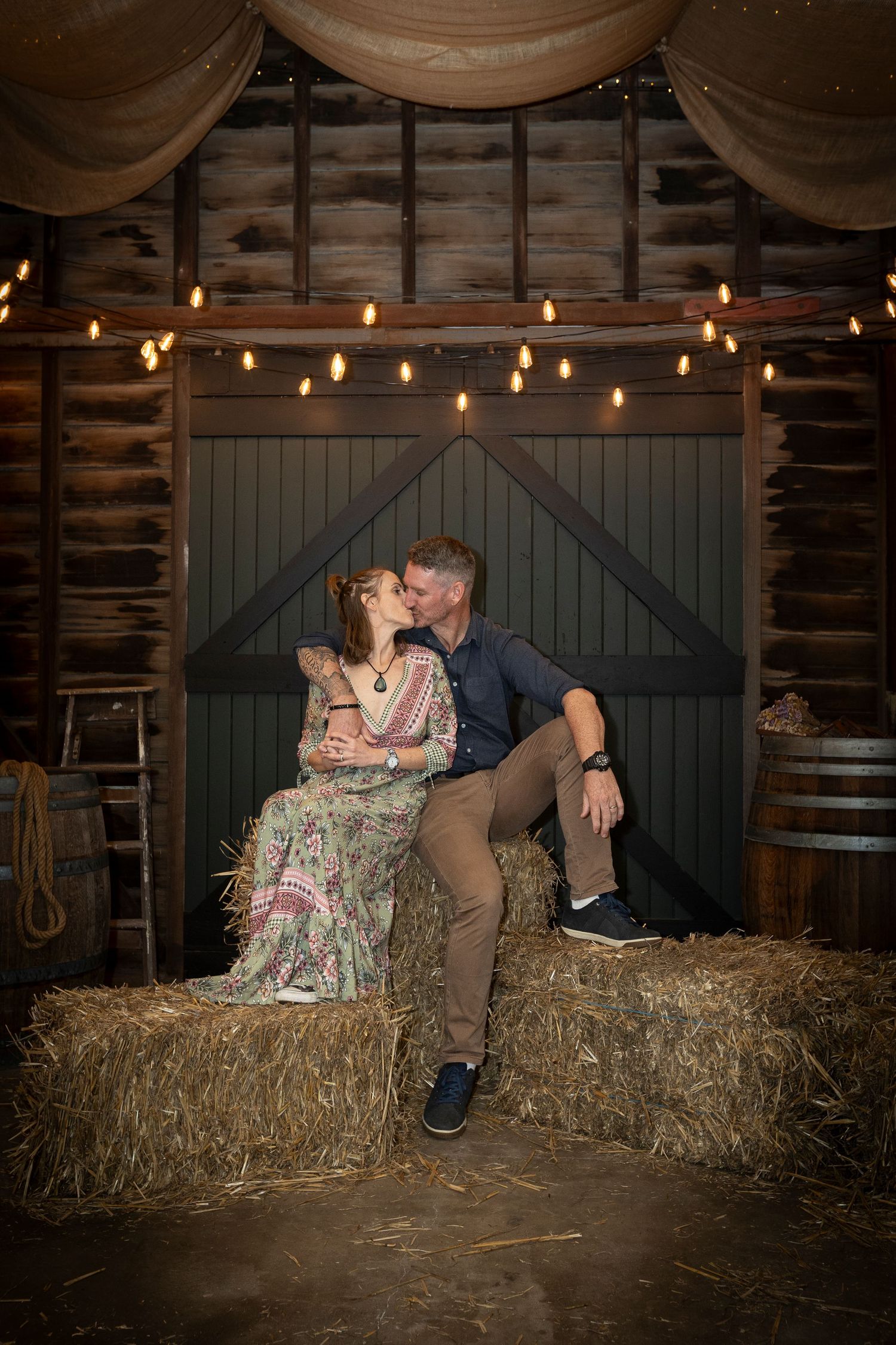 Link to information on Couples Photography Sessions. The photo shows a romantic rustic barn photoshoot with string lights and hay bales