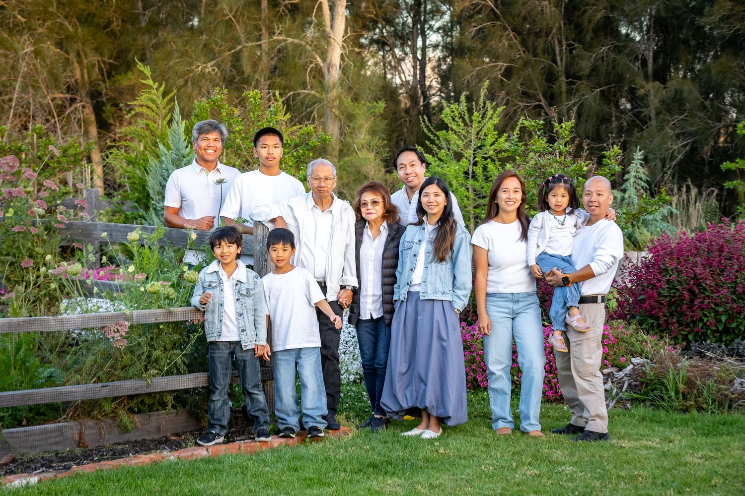 Multi-generational Asian family posing together outdoors in a lush garden setting for a formal family portrait photo.