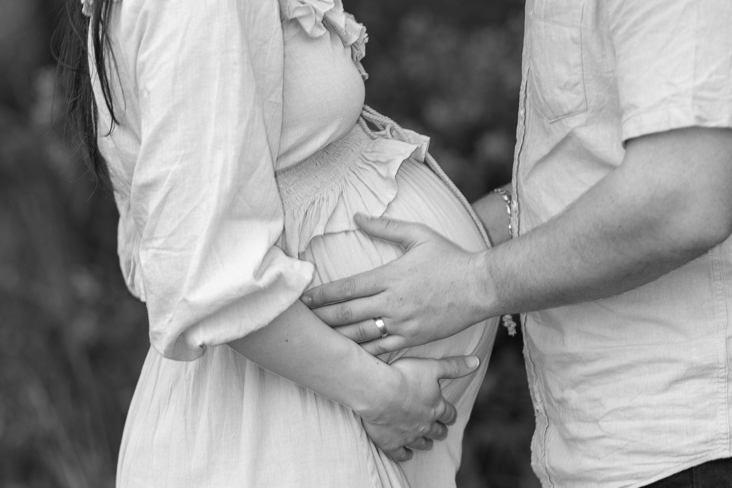 A series of romantic black and white maternity photos showing a couple in white clothing embracing outdoors for a maternity photos