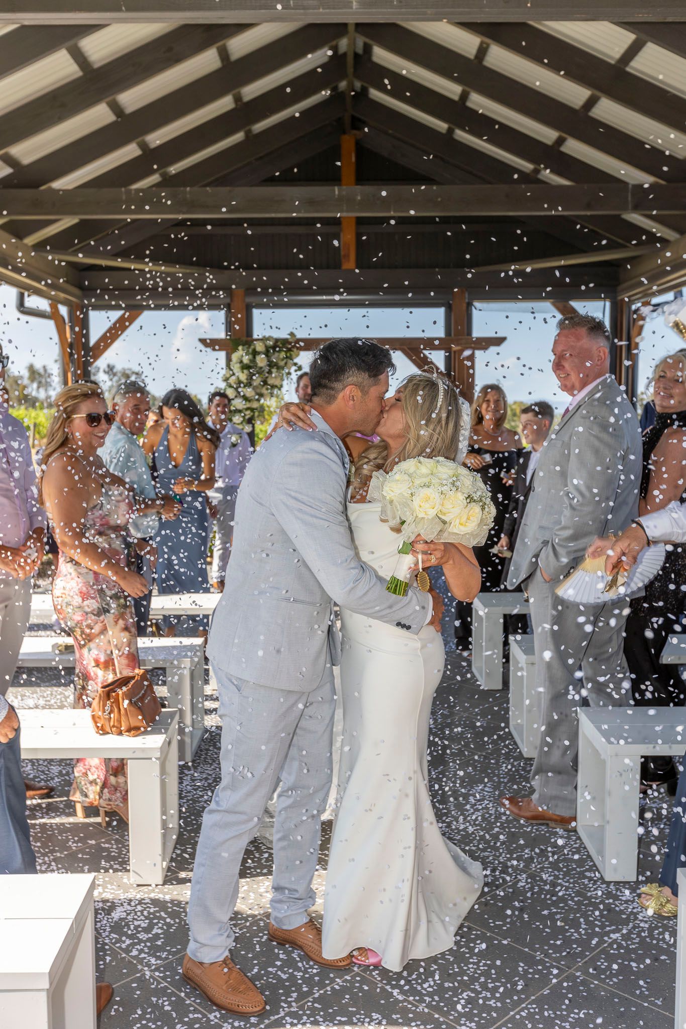 Wedding party celebrates with bubbles under covered pavilion while newlyweds share first dance together.