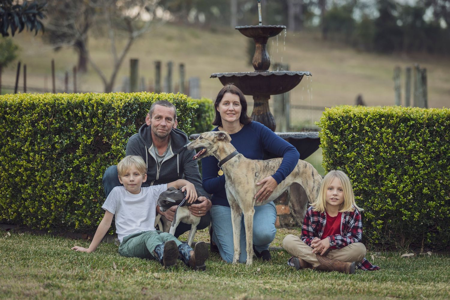 Family poses with their dog near a decorative fountain in a manicured garden.