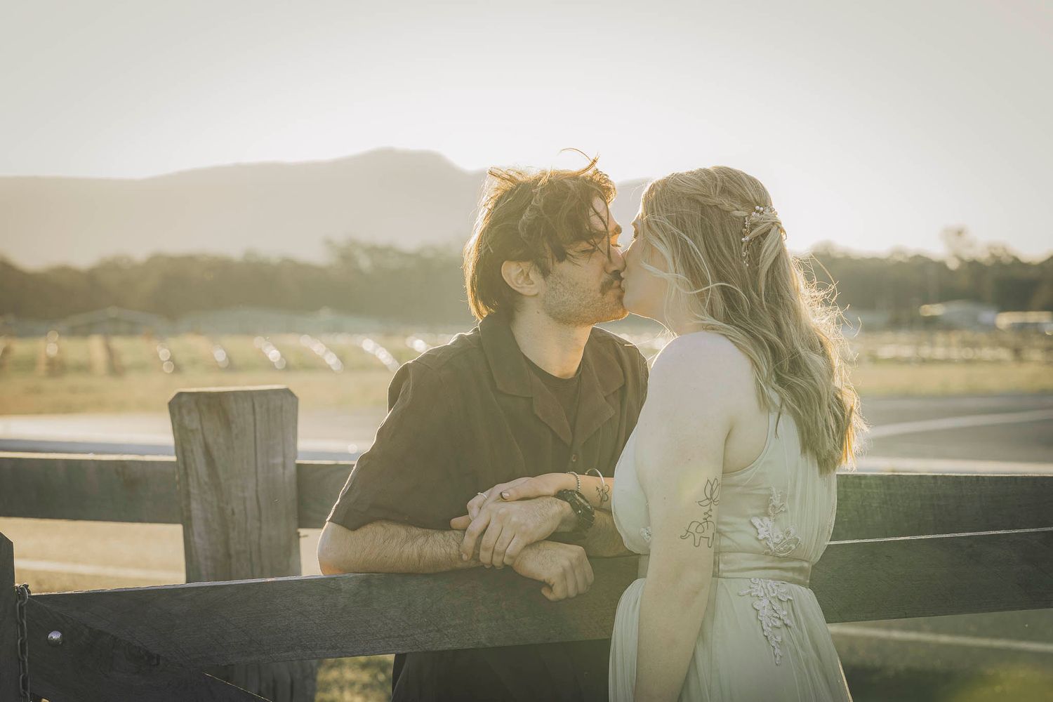A romantic couple embraces during sunset at a scenic overlook with golden light illuminating the scene.