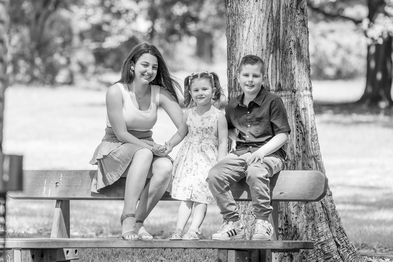 Smiling kids sit together on a park bench in black and white photography during a candid outdoor moment.