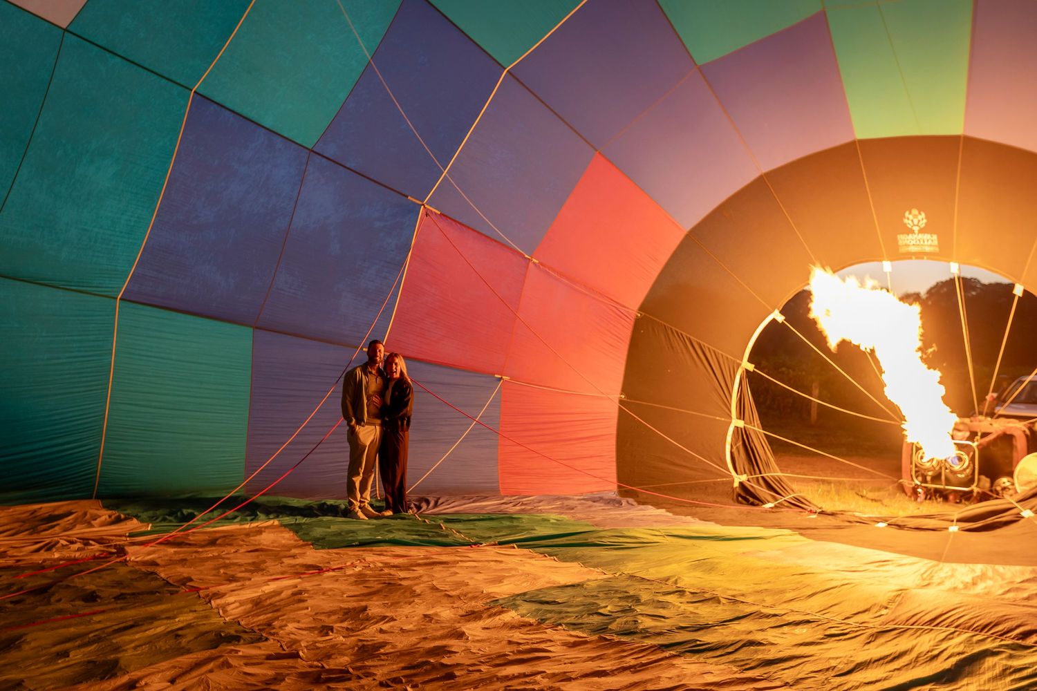 Hot air balloon being inflated at sunset with burners illuminating the colorful fabric against a desert landscape.