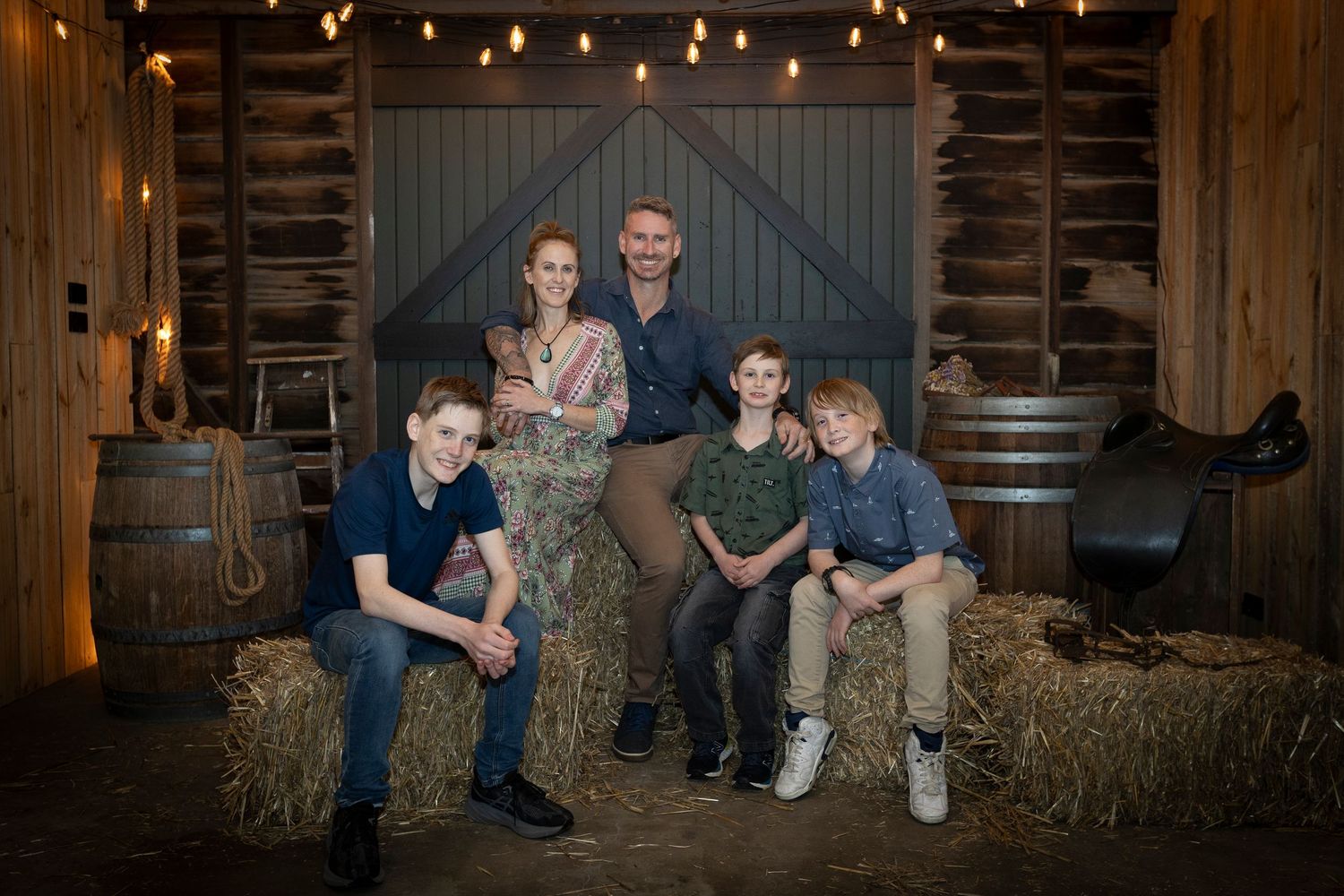 A cozy rustic barn setting with family posing on hay bales under string lights.