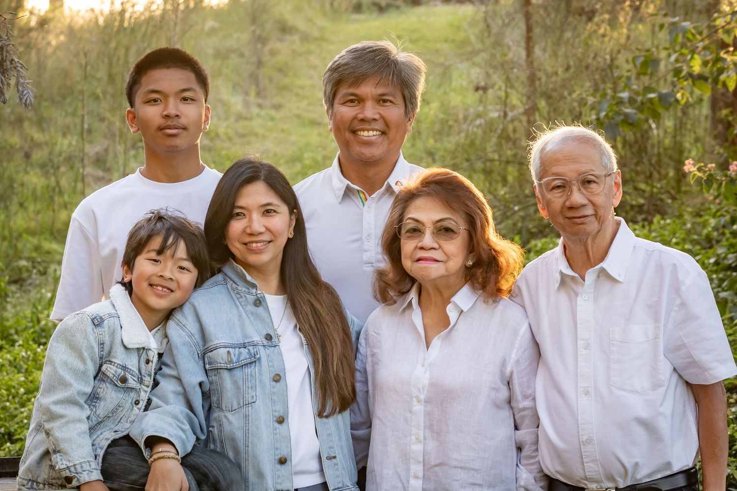 Multi-generational Asian family smiling together outdoors in a sunny green park setting for a portrait photo.