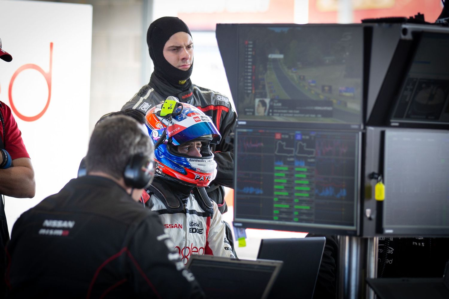 Professional motorsport pit crew working in front of data screens and monitors during a racing event.