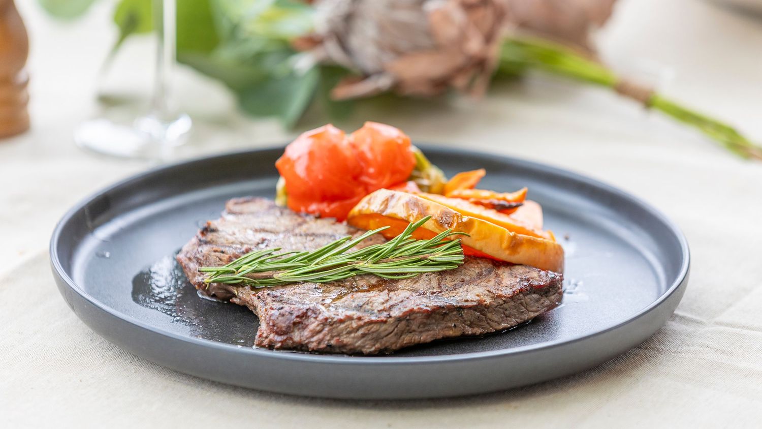Grilled steak served on dark plate with cherry tomatoes, carrots and fresh rosemary garnish.
