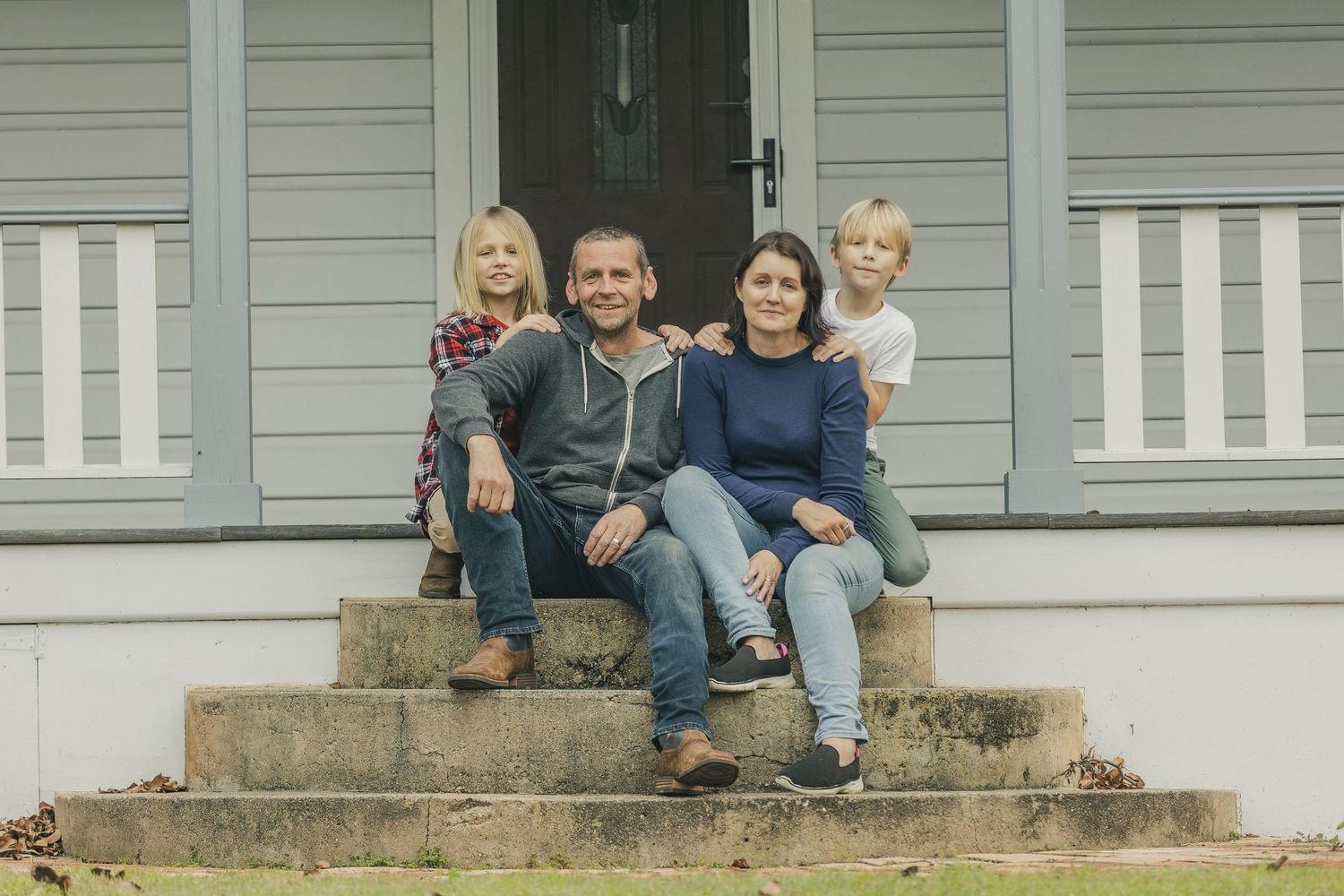 Family gathered on the front steps of a gray weatherboard house.