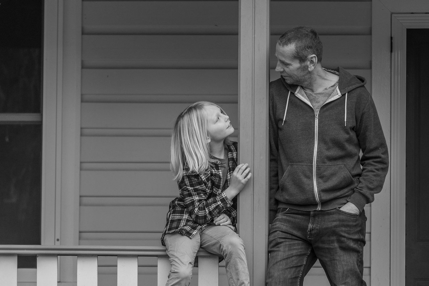 Black and white photo of people sitting on front porch steps of a house.