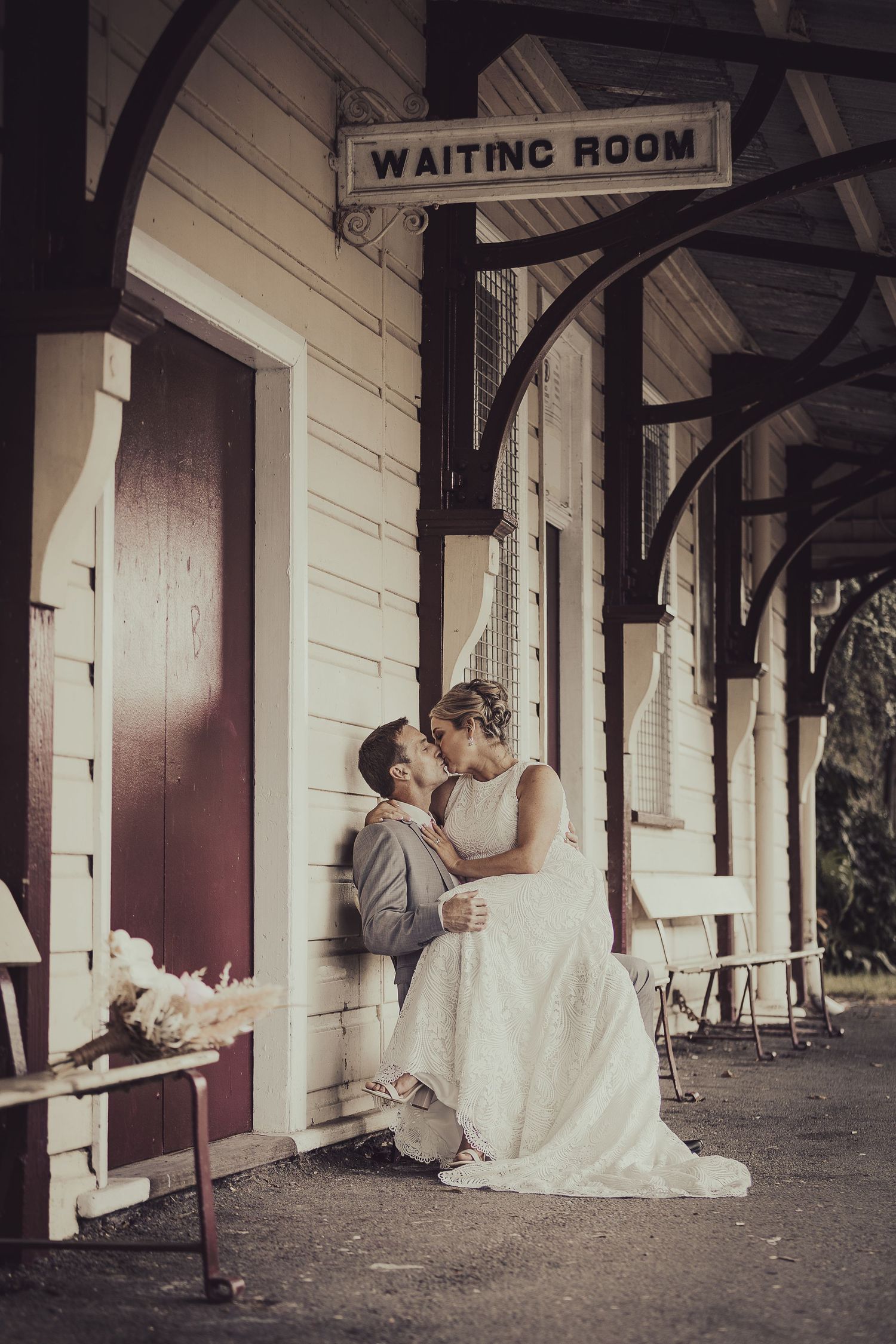 Romantic wedding couple embraces at vintage train station waiting room with rustic white walls and decorative archways.