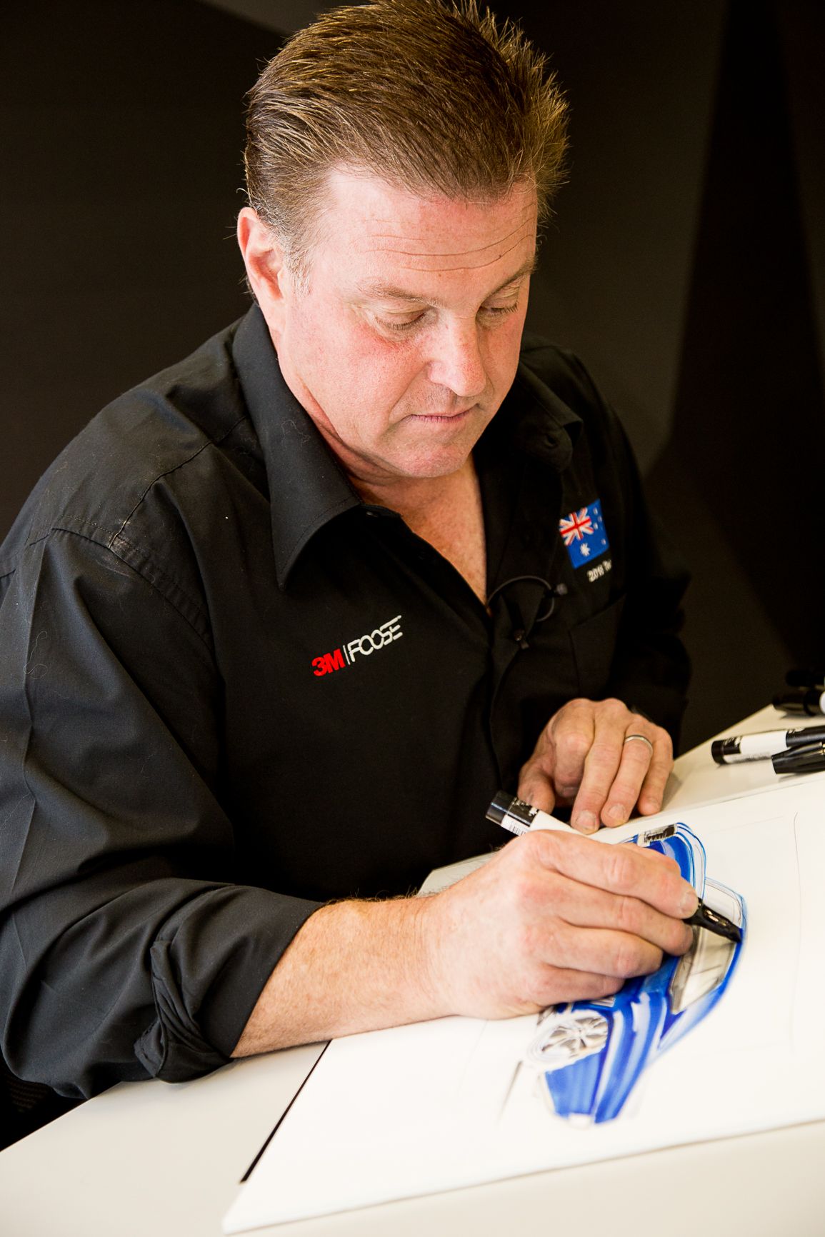 A person wearing a black shirt signs or writes on a white surface in a sequence of four similar photos.