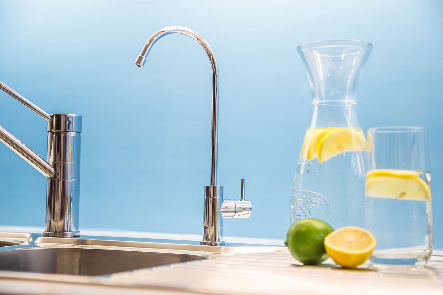 Modern kitchen faucet with water filter system and glass carafes of citrus-infused water on counter.