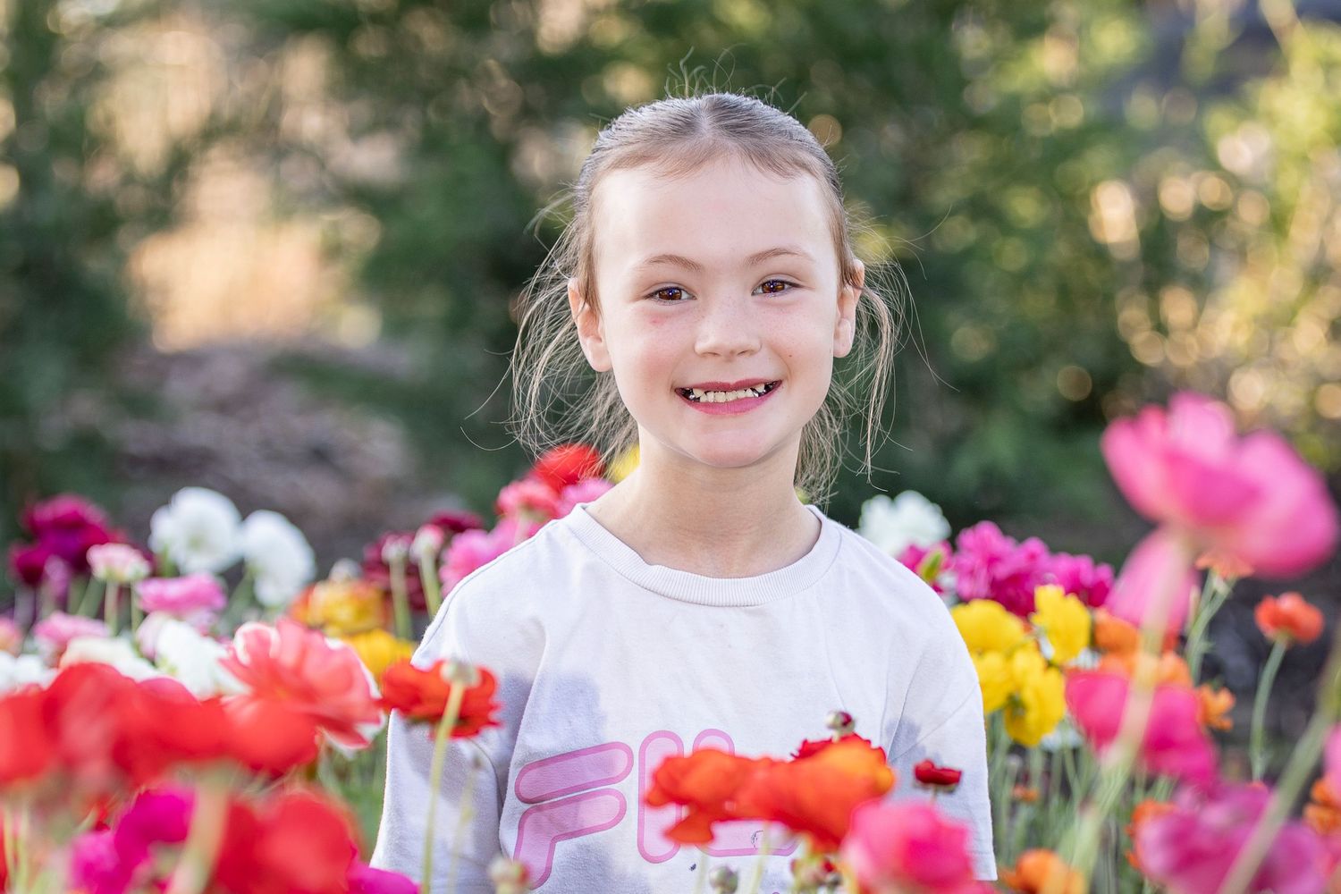 A young child smiles joyfully while standing among vibrant red and pink tulips in a spring garden.