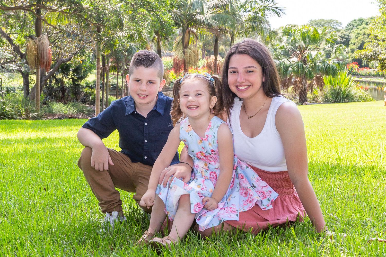 A family group poses together on green grass during a sunny outdoor photo session.