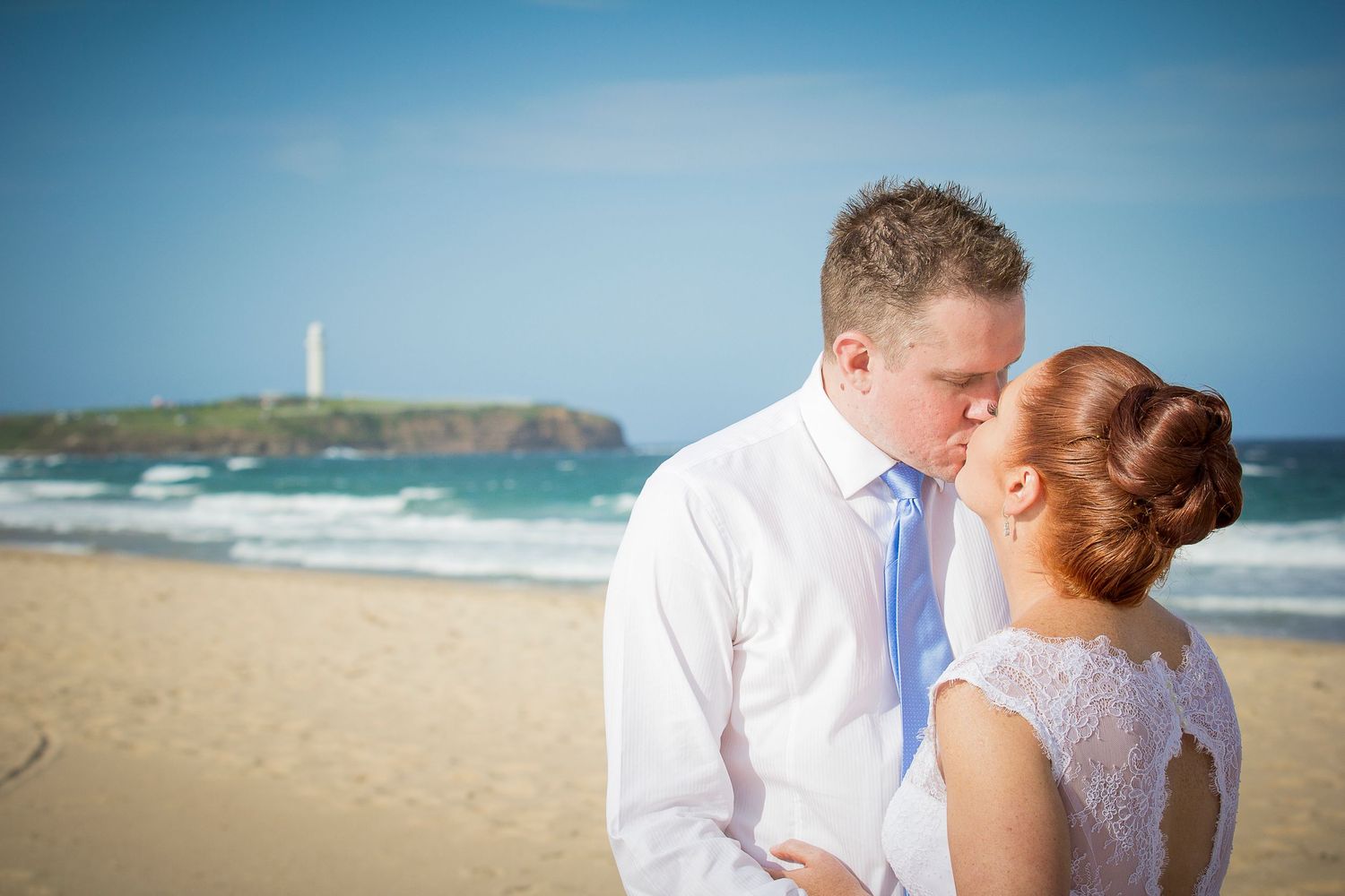 A romantic beach wedding scene with a lighthouse in the background on a beautiful sunny day.