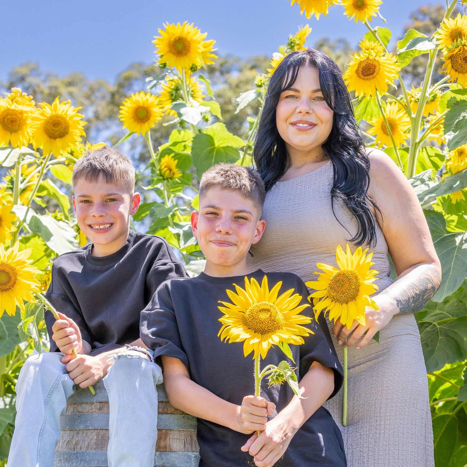 Family wearing black and gray outfits pose together in a vibrant sunflower field on a sunny day.