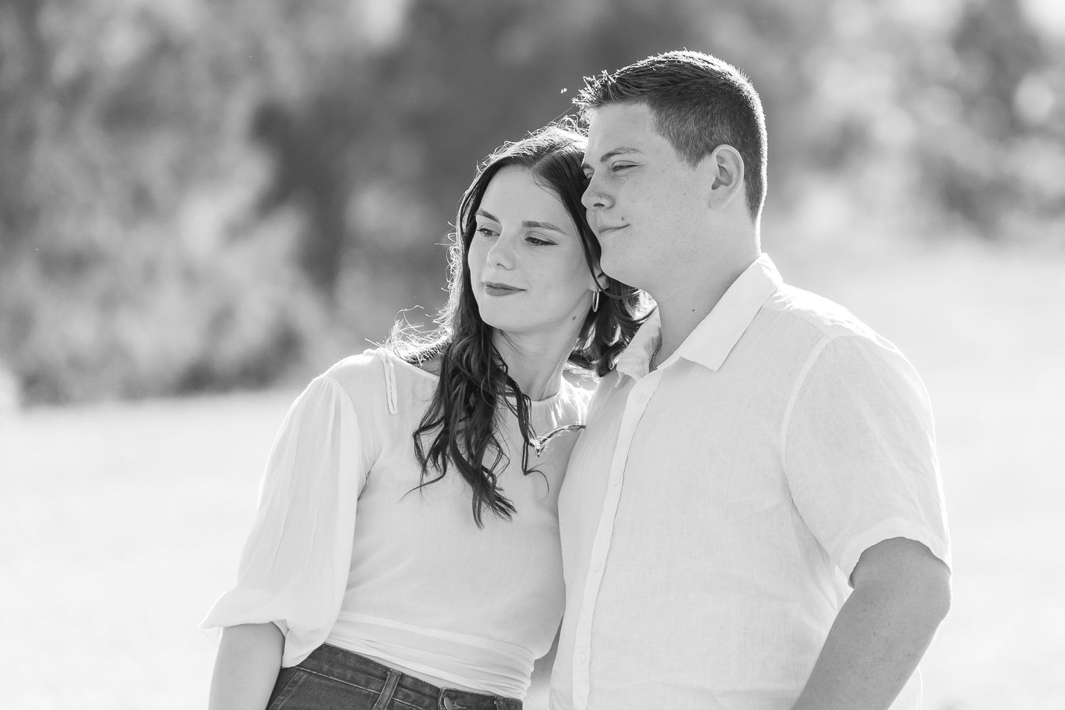 A romantic black and white portrait of a couple in casual white shirts sharing an intimate moment outdoors.