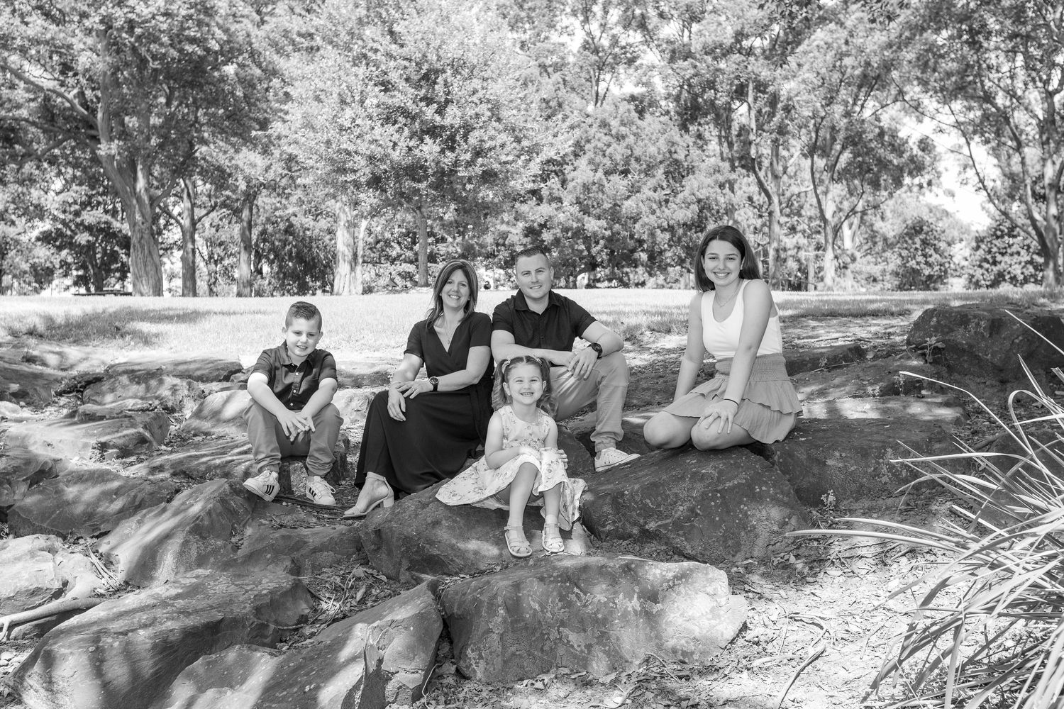 People relax and gather outdoors in a park setting with rock formations and trees providing a natural backdrop.