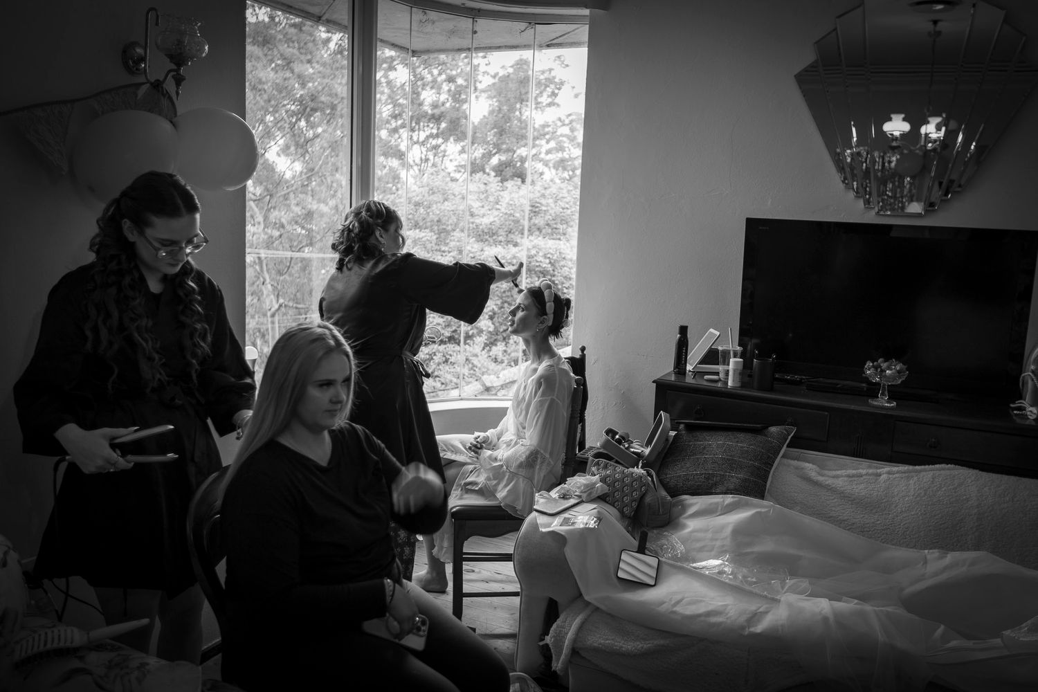A black and white photos showing a bride having her make up applied in front of a window