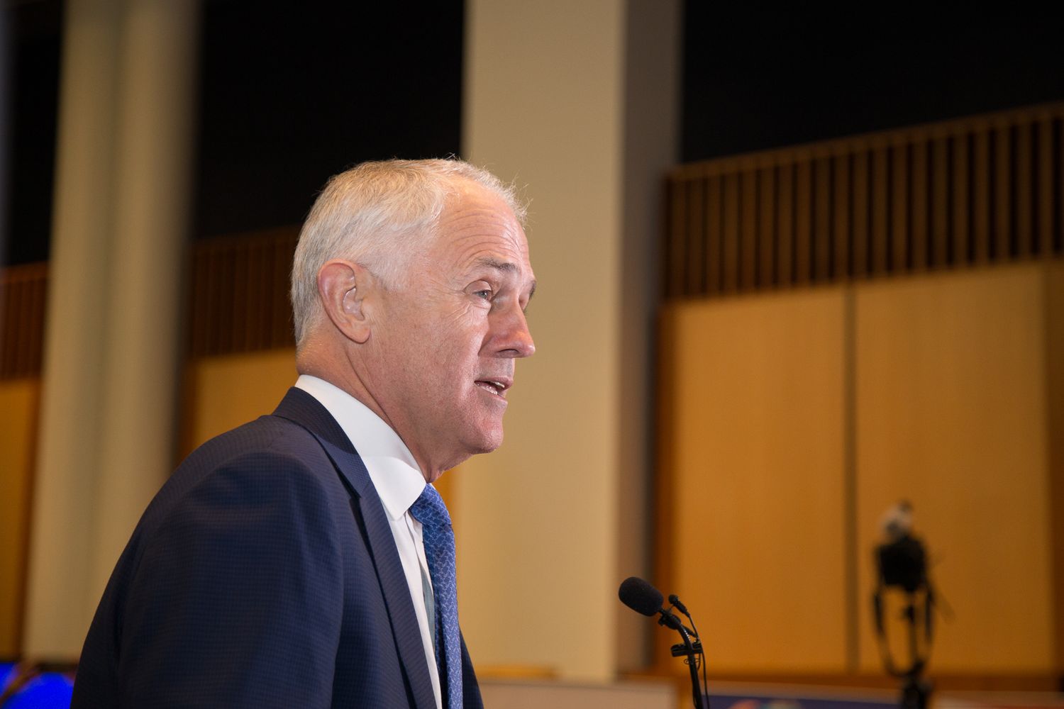 The prime minister of Australia, Malcolm Turnbull. Speaks at a podium in a room with wooden balcony railings visible in the background.