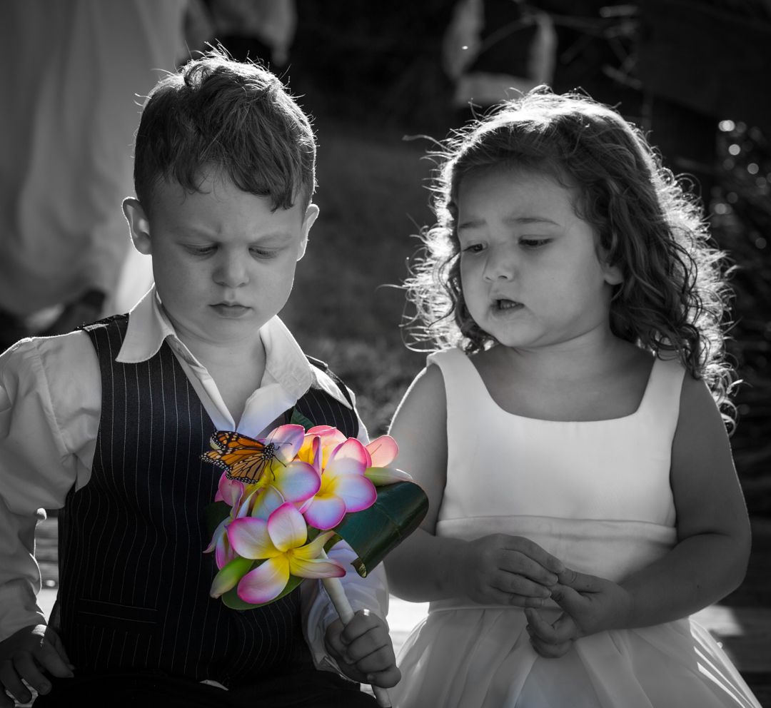 Two young children looking at a colorful bouquet of flowers in a black and white photo with selective color.