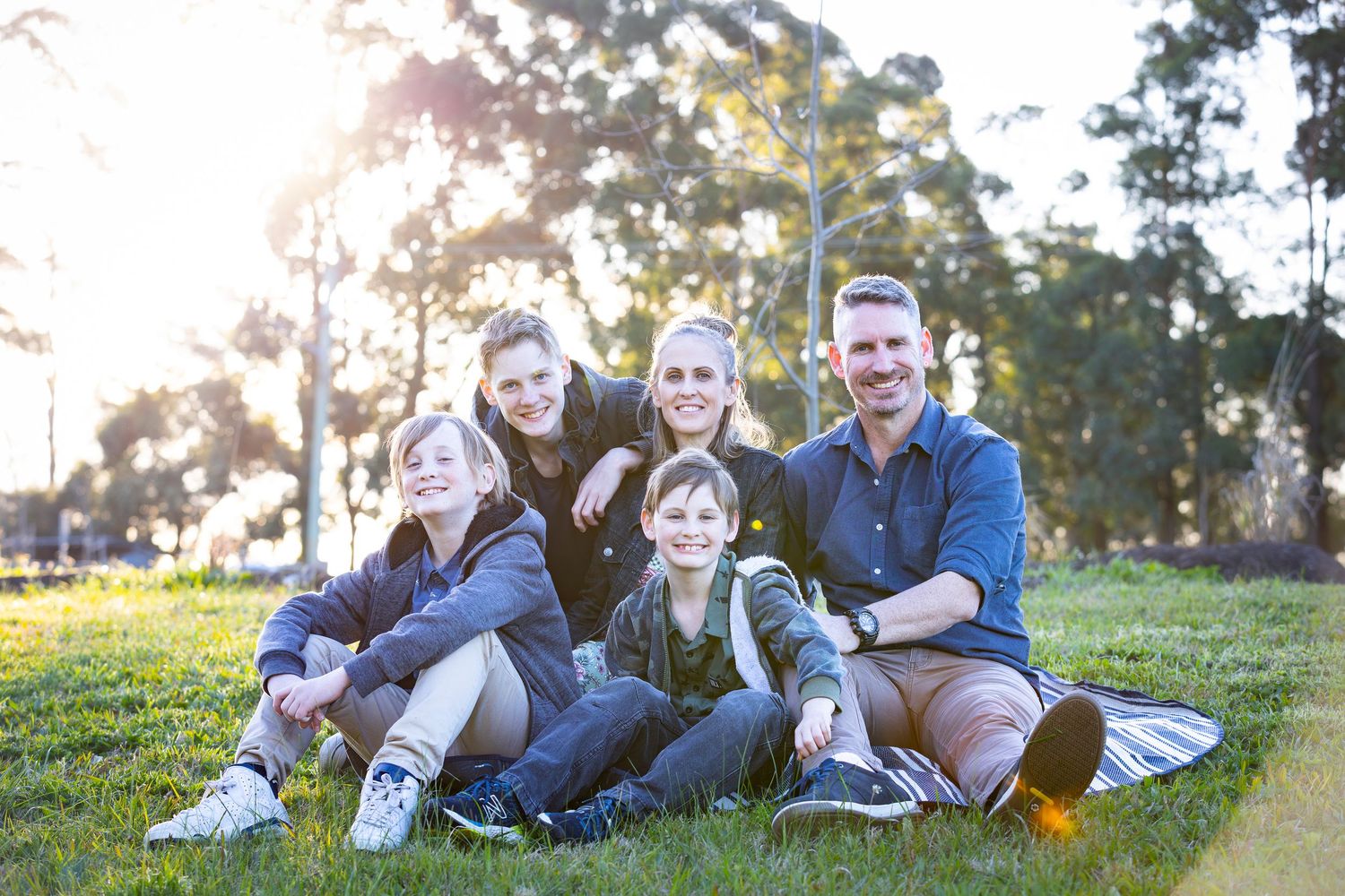 Family sitting together on blanket in sunny park setting.