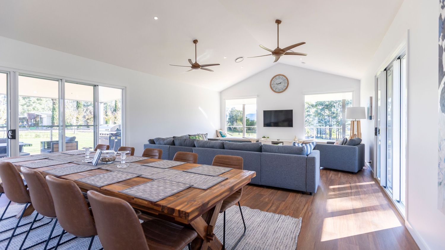 Modern open concept living area with wooden dining table, grey sectional sofa and large windows bringing in natural light.