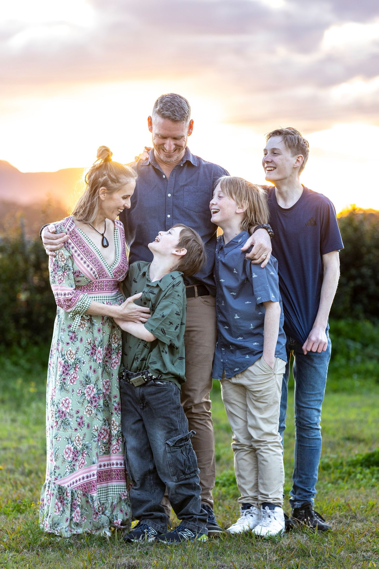 Family group standing together in a grassy field during golden hour sunset.